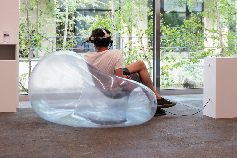 Ein Mann sitzt auf einem durchsichtigen Sessel und hat ein VR-Headset auf