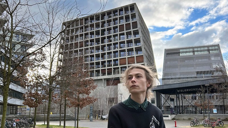 Maksym sitzt vor dem Helsinki-Gebäude und der HGK Basel. Dieses Bild ist nicht KI-generiert.