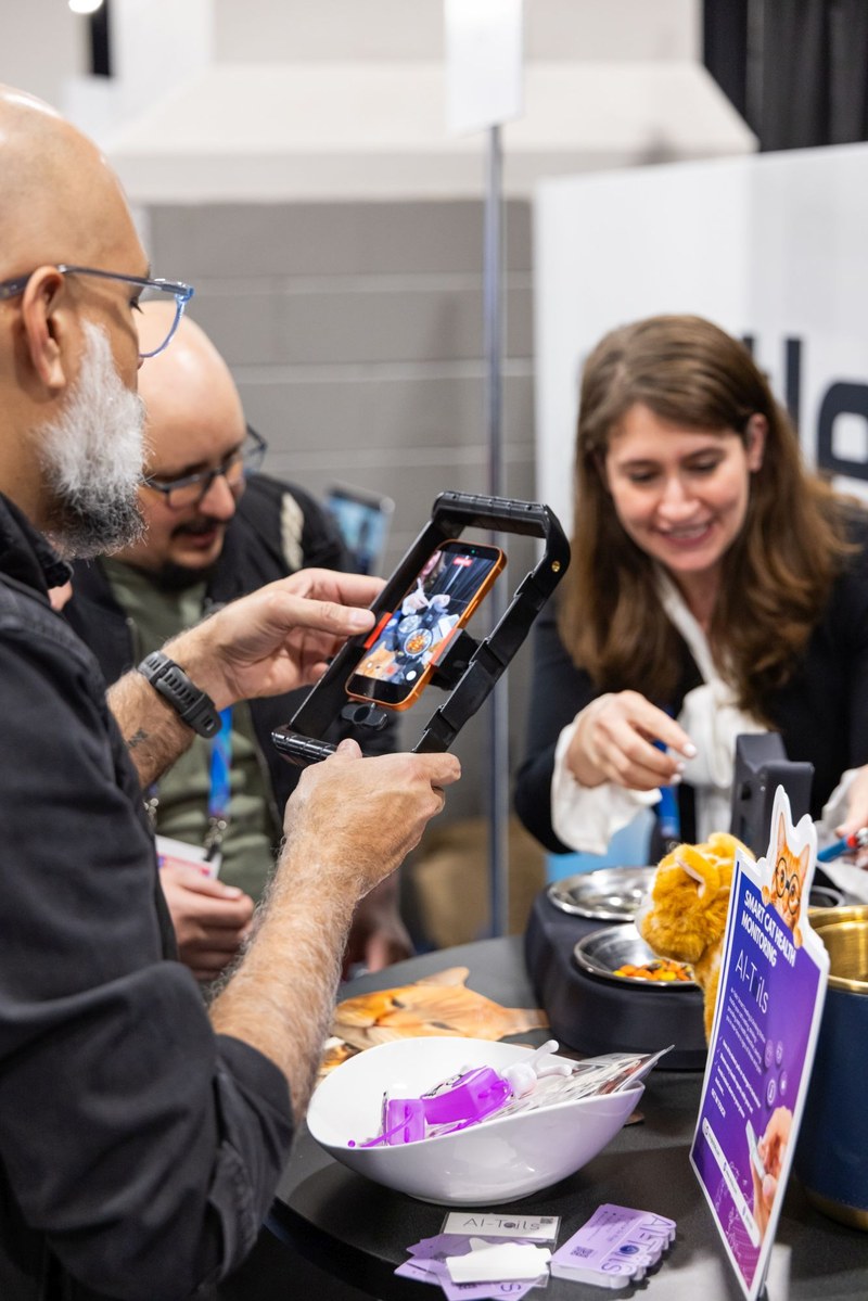 Angelica de Riggi erklärt Messebesuchern AI Tails One. Im Vordergrund sieht man einen Besucher, der mit seinem Handy das Produkt fotografiert