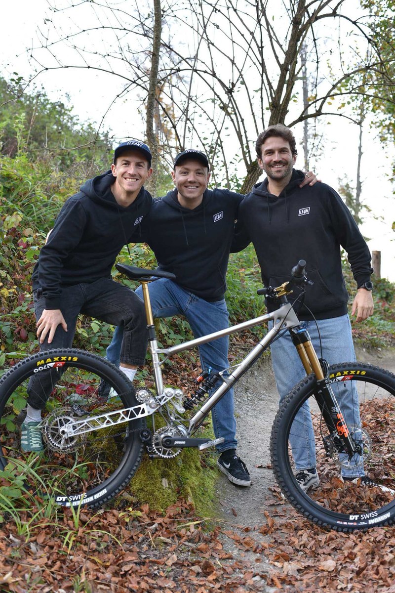 Die drei stehen hinter dem Enduro-Bike und fassen sich an die Schultern