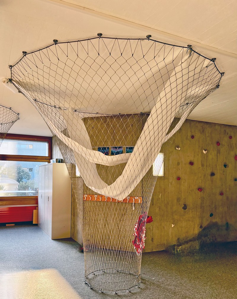 Ein horizontal gespanntes Netz hängt etwa 2 Meter über dem Boden. Im Netz ist ein grosser Ring von 50 Zentimeter Durchmesser eingeflochten, durch den man Klettern kann.