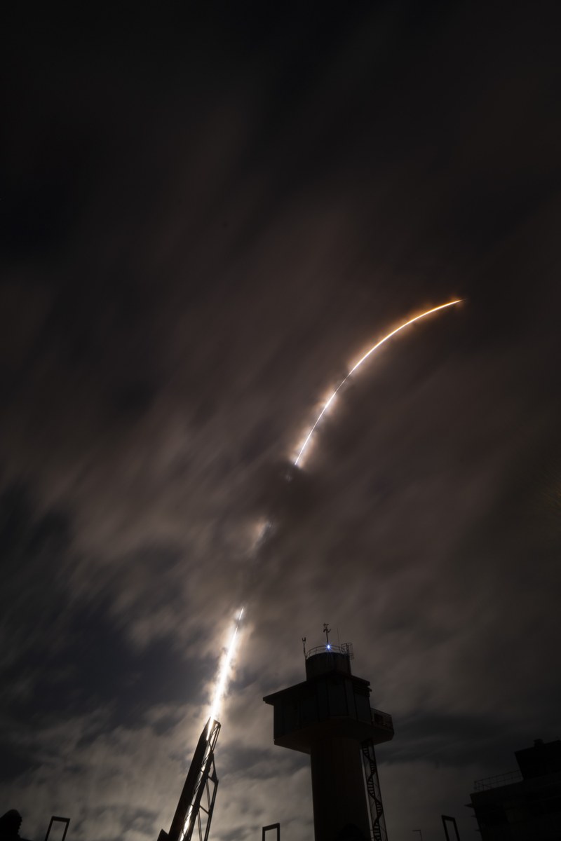 Der Feuerschweif der Rakete vor dunklem Nachthimmel und die Schattenumrisse eines Kontrollturms