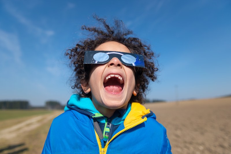 Ein Kind mit offenem Mund und einer Sonnenfinsternisbrille