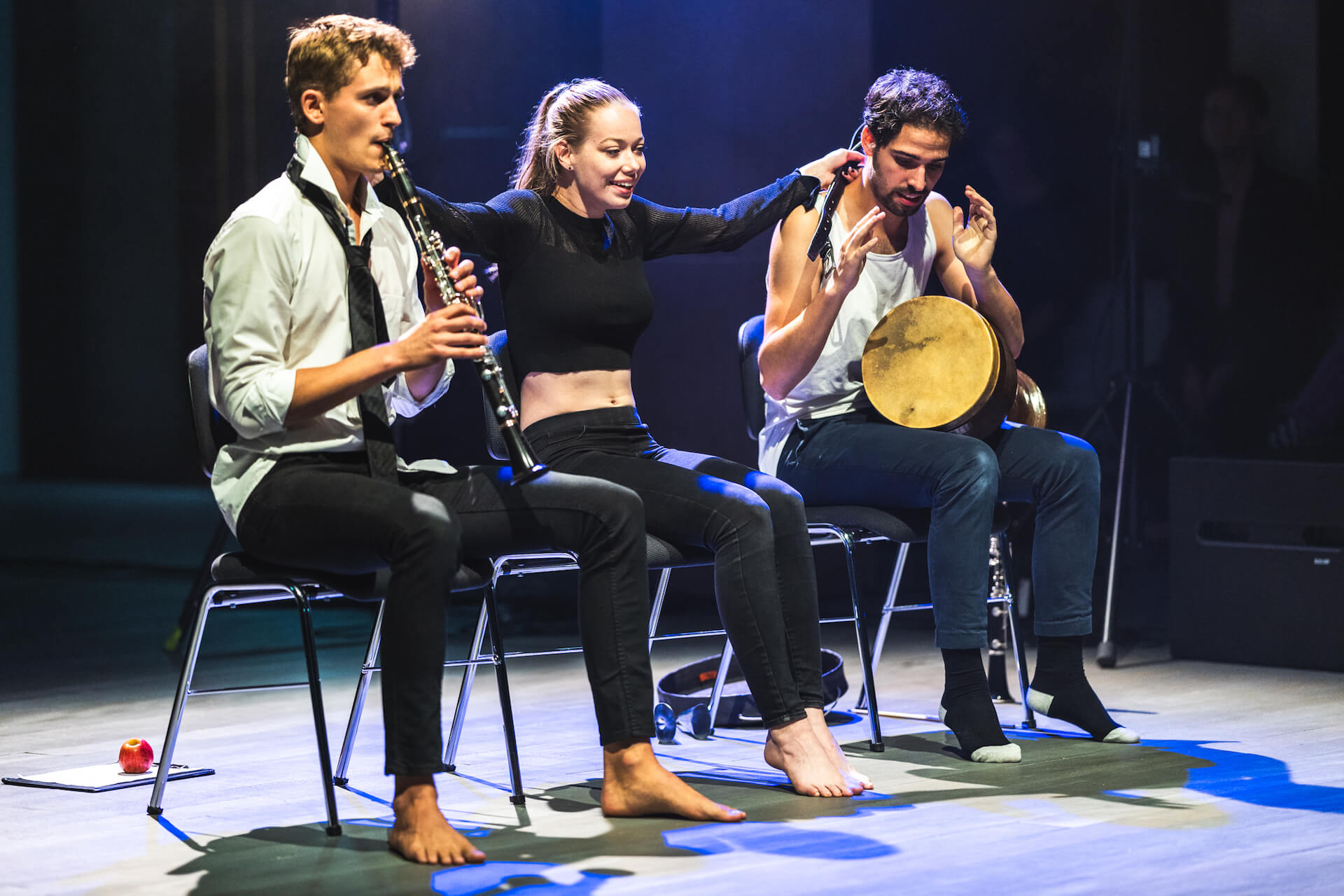 Performance; links sitzt ein Klarinettist, rechts ein Djembe-Spieler und in der Mitte eine Sängerin