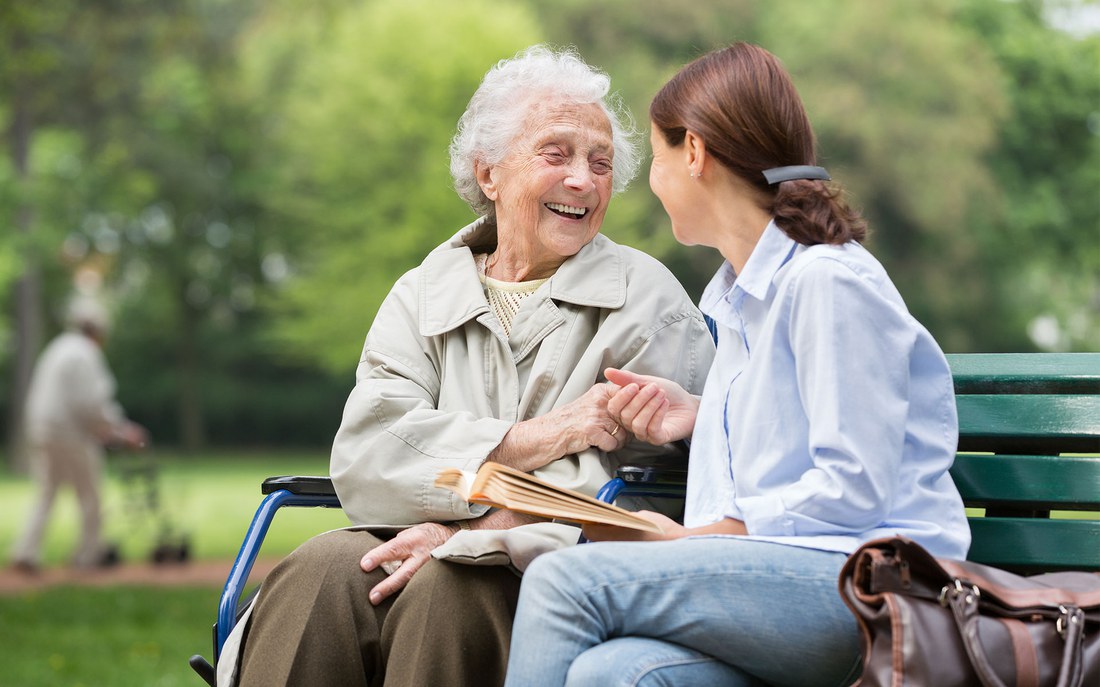 Eine ältere Frau sitzt mit einer Betreuerin auf einer Parkbank.  (© FredFroese/E+/Getty Images)