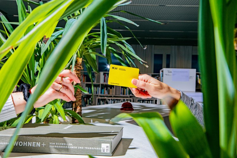 Eine Hand reicht einer anderen Hand die FH-Card im FHNW-Gelb