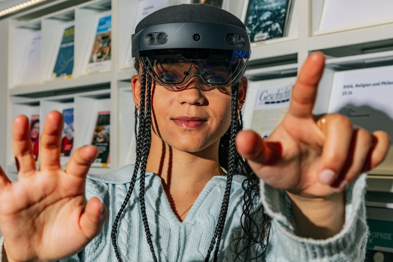 Eine junge Frau mit einem VR-Headset macht eine Tipp-Geste in die Kamera