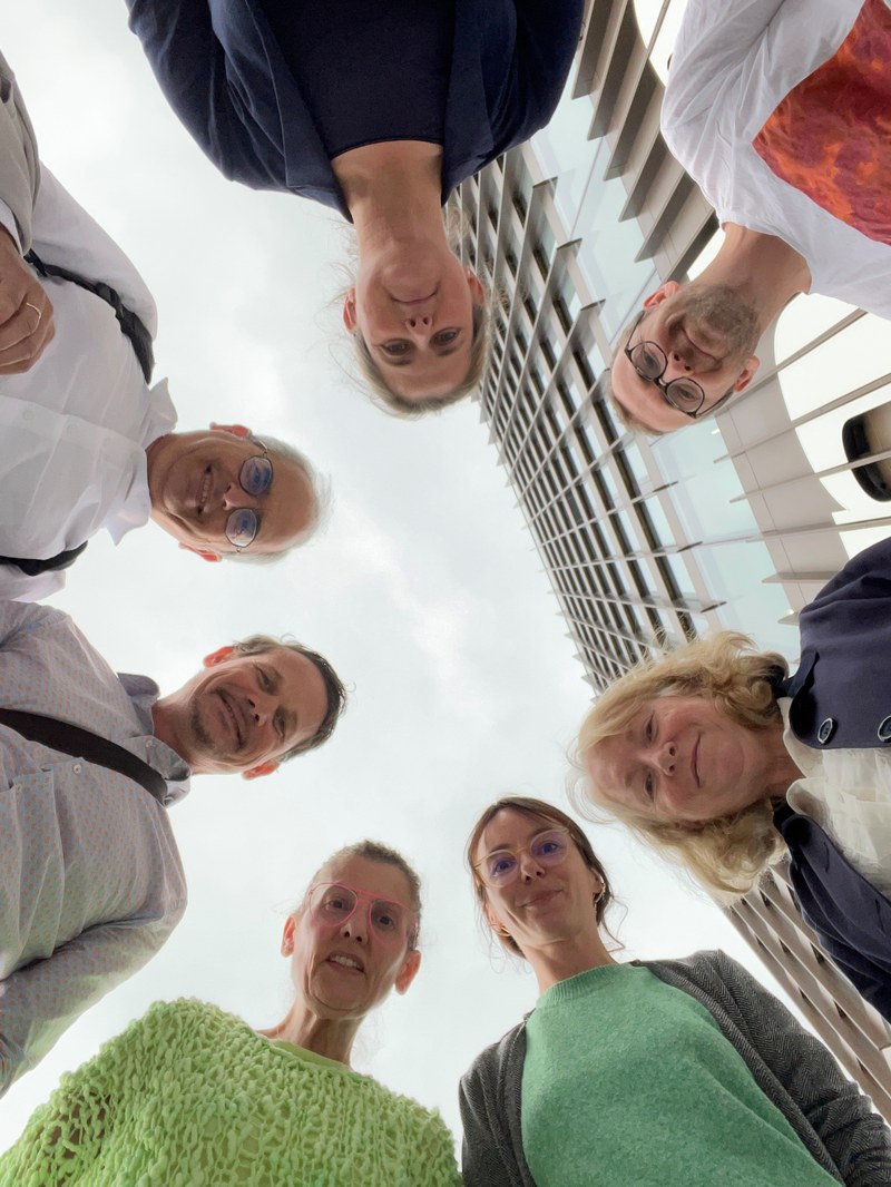 Teilnehmnde der Summer School  stehen im Kreis. Sie sind von unten fotografiert und gucken von oben in die Kamera