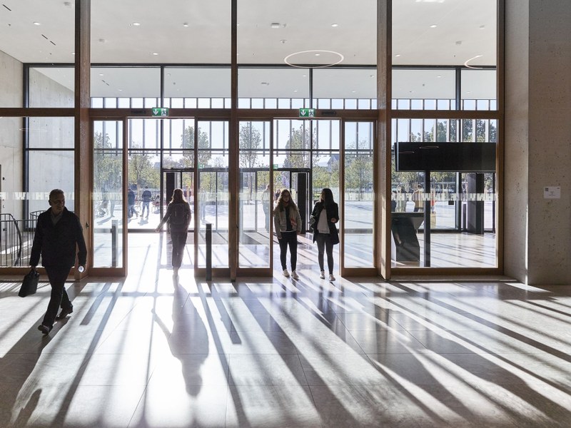 Leute betreten den FHNW Campus Muttenz, im Gegenlicht so dass man die langen Schatten sieht
