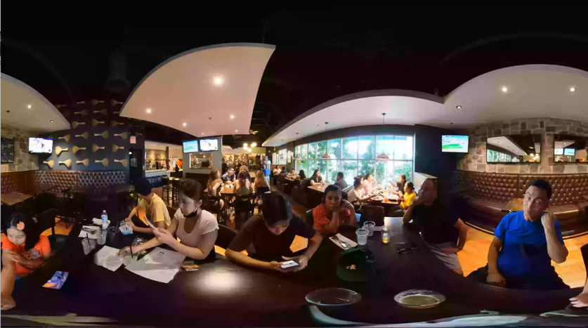Ein Tisch in einem belebten Restaurant, wie er in der Virtual-Reality-Umgebung aussieht. Viele Personen sitzen dem Betrachter gegenüber und stehen für die vielen Reize, für die trainiert wird.