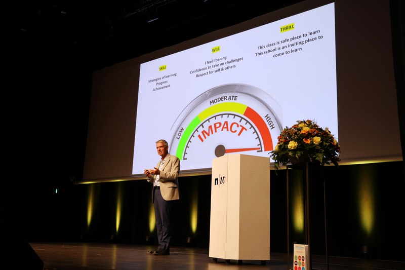 John Hattie spricht auf der Bühne. Im Hintergrund zeigt die Leinwand die typische Abbildung für die Effektstärke.