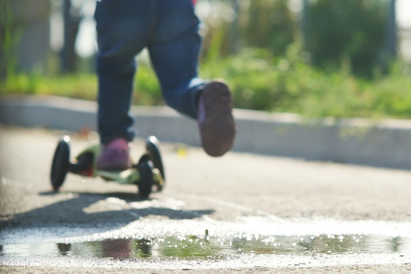 Ein Kind fährt auf einem Trottinett auf der Strasse.