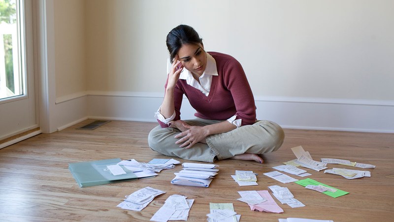 Frau sitzt am Boden mit vielen unbezahlten Rechnungen vor sich ausgelegt.