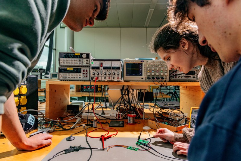 Eine junge Frau und zwei Männer arbeiten an einem Elektrotechnik-Projekt