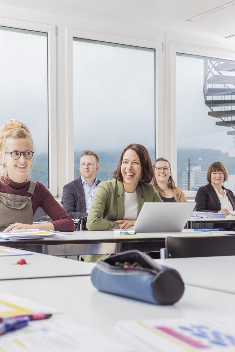 A laughing woman sits behind a laptop