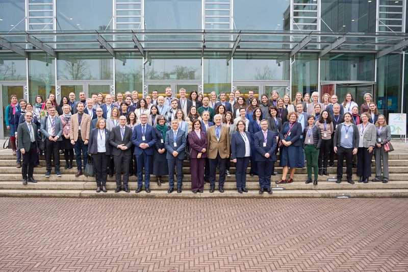 Directors and staff standing on stairs in front of a glass building. It is a group of ca. 50 people