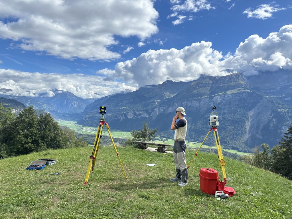 Aufgebautes Reflektorstativ und Tachymeter mit Weitblick über Meiringen im Berner Oberland.