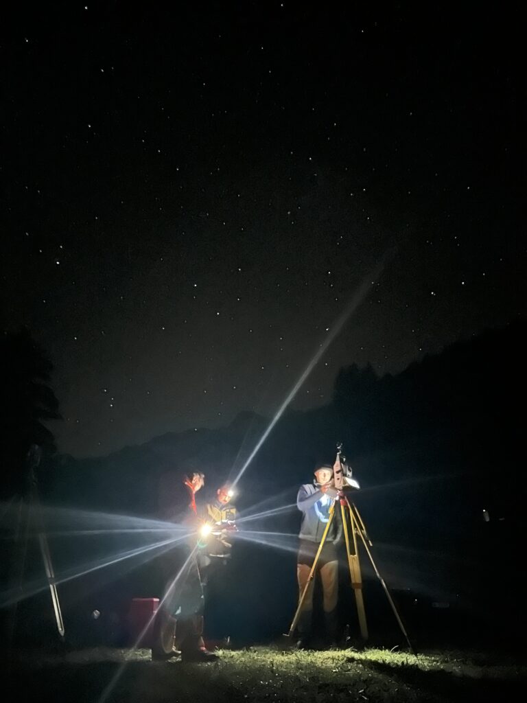 Nachtmessung mit Taschenlampe und Tachymeter unter klarem Sternenhimmel.