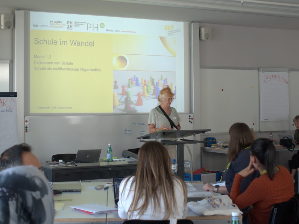 Bild einer RILF-Dozentin in einem Klassenzimmer frontal und die Rücken der RILF-Studierenden, die nach vorne Blicken